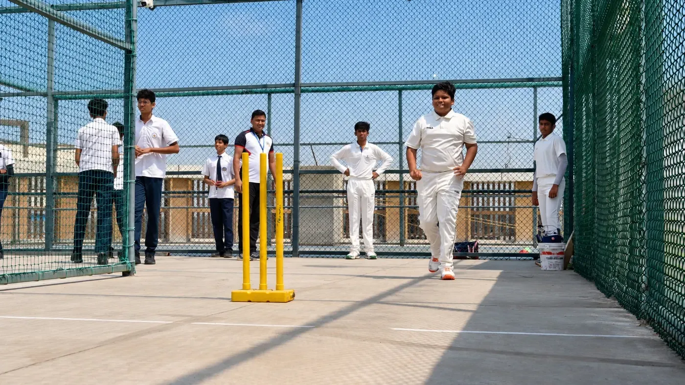 Student bowling in the cricket nets with a coach and teammates